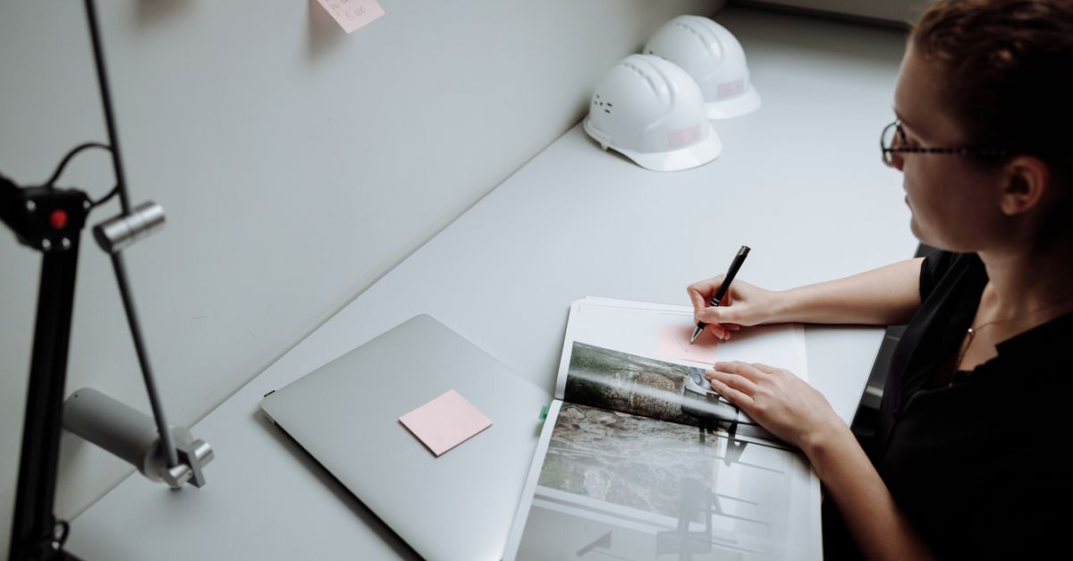 Professional architect making notes in a modern office with a laptop and safety helmets.